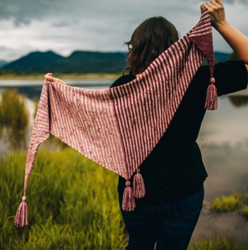 woman standing by water putting on hand knit shawl